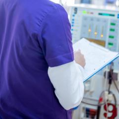 Doctor in purple gown with clipboard in front of machine